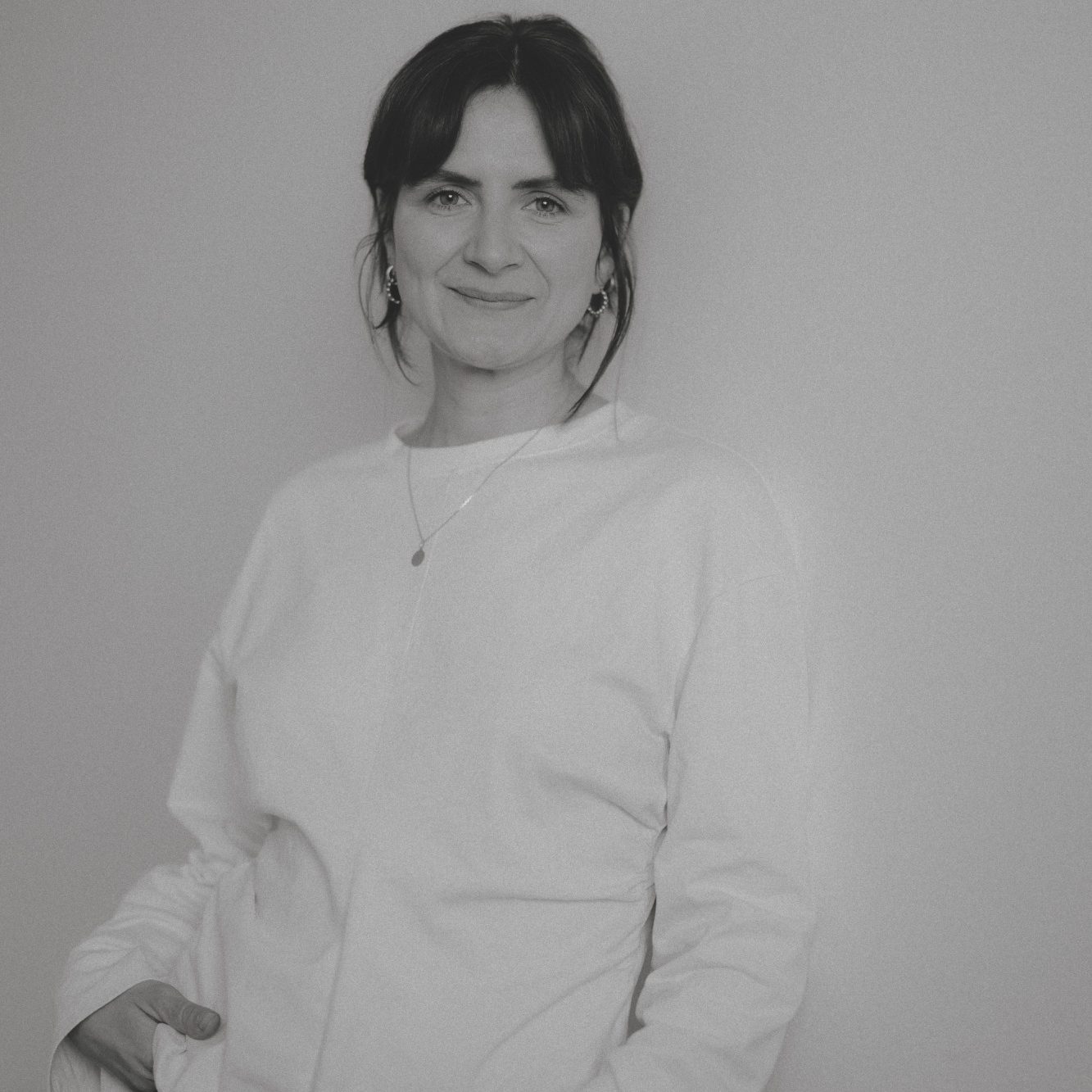 Hannah Waeny - doulannah Bild von Hannah Waeny (doulannah) vor einer weißen Wand mit freundlichem Blick und einem sanften Lächeln.